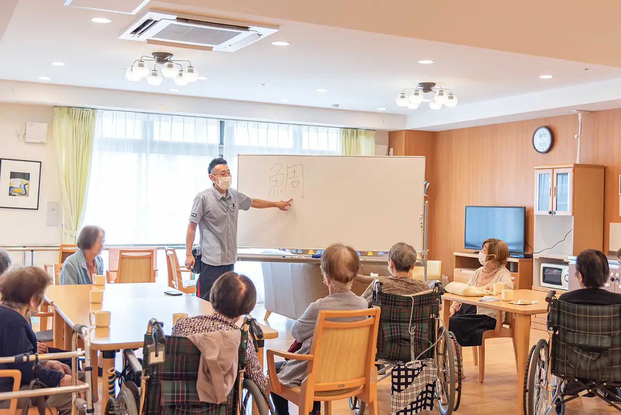 職員による講座・教室の様子。複数の入居者が講師の説明を聞いている。