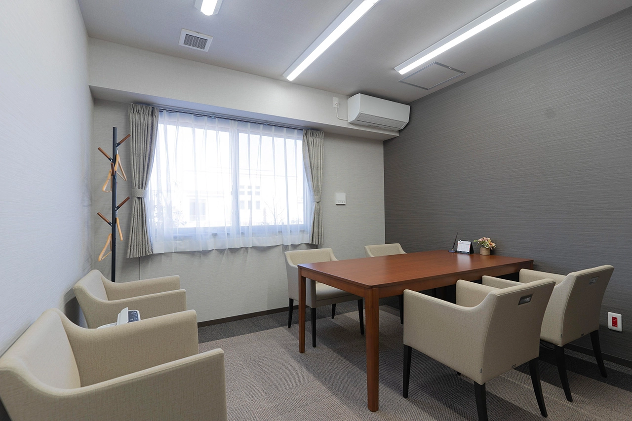 木製テーブルと複数のソファが配置された明るい共用談話室。窓からの採光と照明で快適な空間。