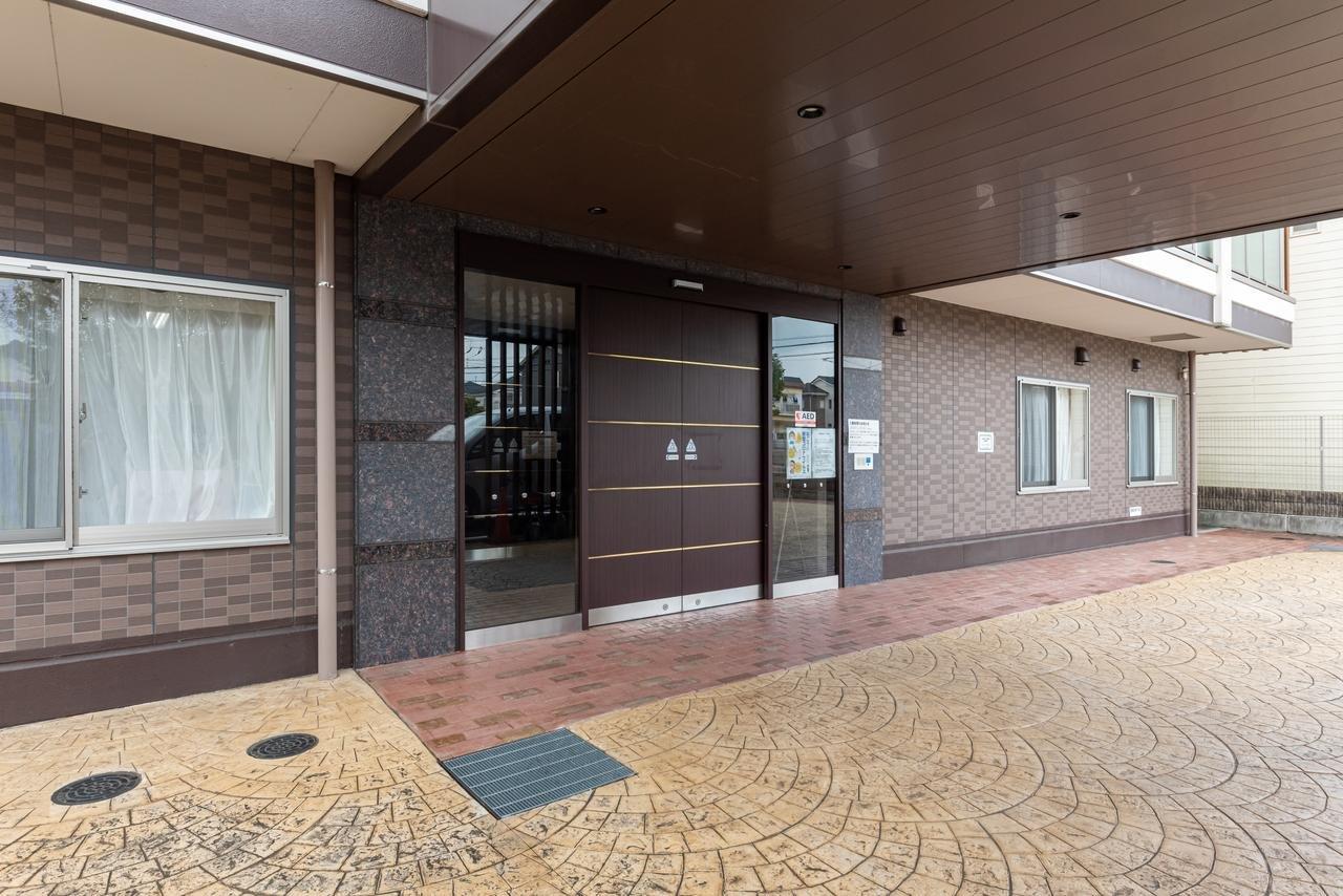 介護施設の玄関・車寄せ。茶色系のタイル張りの建物外壁と広々とした駐車スペース付きアプローチ。