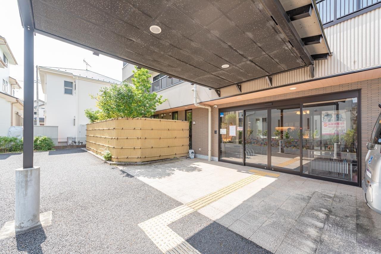 施設の玄関・車寄せ。屋根付きの広い外部スペースと大型ガラス扉が見える。
