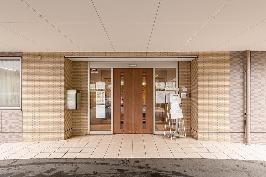 茶色いタイル張りの建物の玄関。木製ドアと案内板が見える