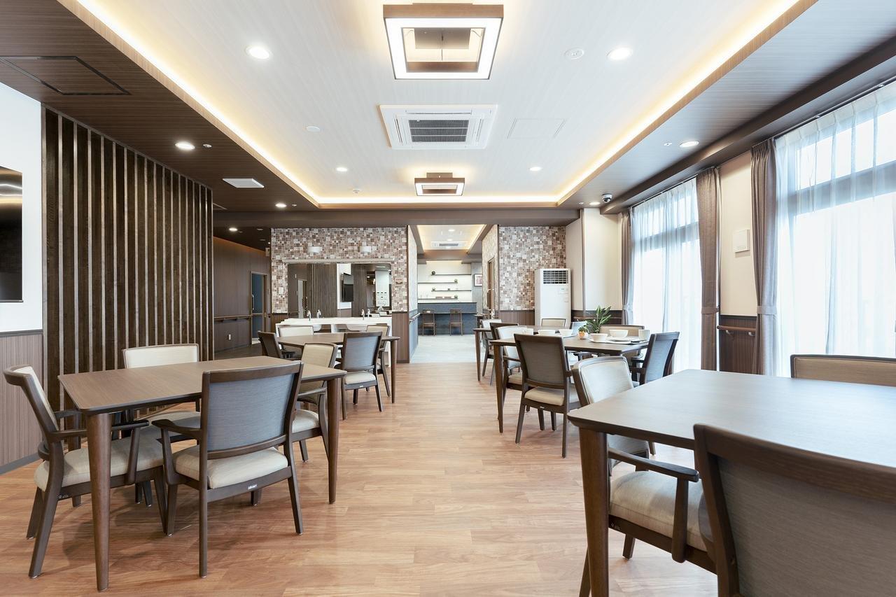 木調でモダンな食堂。複数のテーブル席と奥にキッチンカウンター、大きな窓から採光。