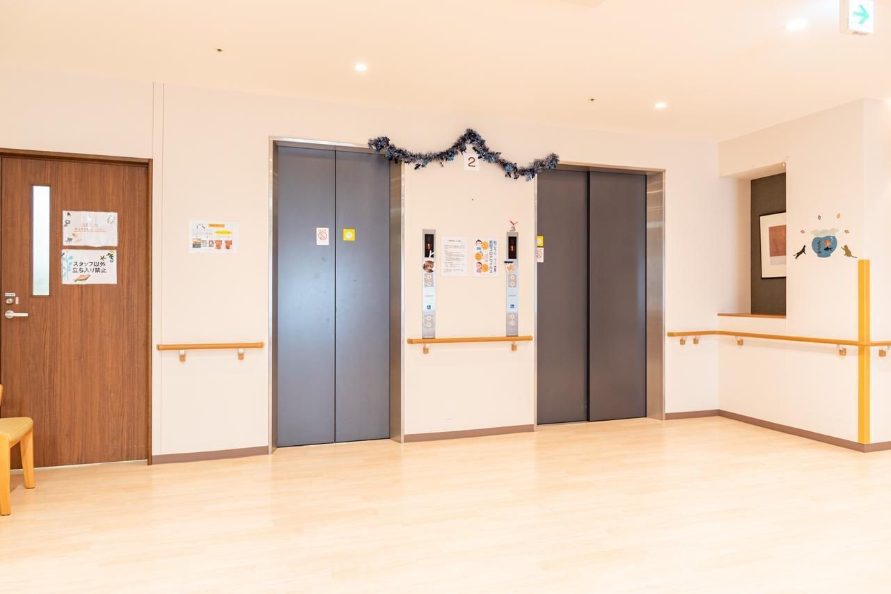 介護施設の共用スペース。エレベーターと掲示板、クリスマス装飾がある廊下。