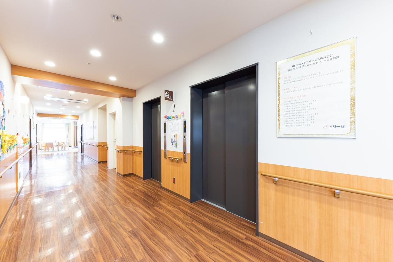 介護施設のロビー・廊下。エレベーター、掲示板、木調の温かみのある内装。